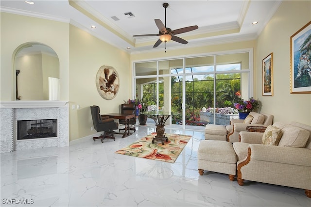 living room featuring a fireplace, ceiling fan, a tray ceiling, and ornamental molding