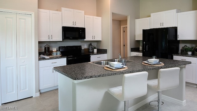 kitchen featuring sink, an island with sink, a breakfast bar, white cabinets, and black appliances