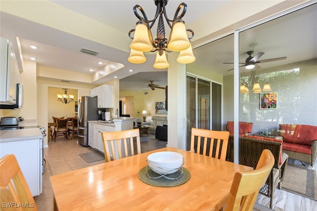 tiled dining room featuring a raised ceiling and ceiling fan with notable chandelier