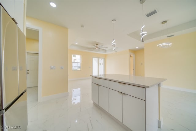 kitchen featuring ceiling fan, a kitchen island, white fridge, white cabinetry, and decorative light fixtures