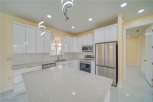 kitchen featuring light stone counters, stainless steel appliances, white cabinetry, hanging light fixtures, and sink