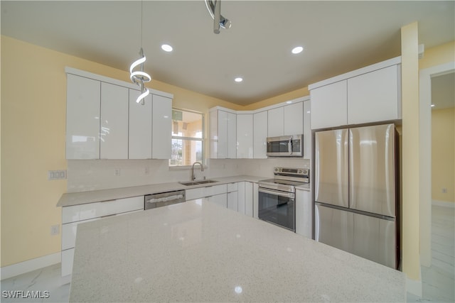 kitchen featuring stainless steel appliances, sink, light stone countertops, white cabinets, and pendant lighting