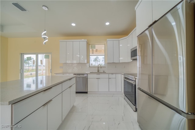 kitchen featuring stainless steel appliances, white cabinetry, sink, backsplash, and pendant lighting