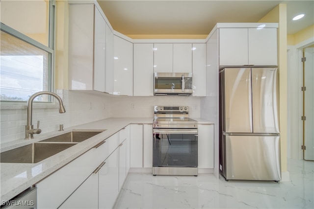 kitchen featuring stainless steel appliances, white cabinetry, sink, light stone countertops, and backsplash