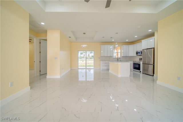 kitchen featuring appliances with stainless steel finishes, a raised ceiling, hanging light fixtures, white cabinets, and a center island