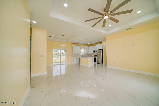 unfurnished living room featuring ceiling fan, sink, and a tray ceiling