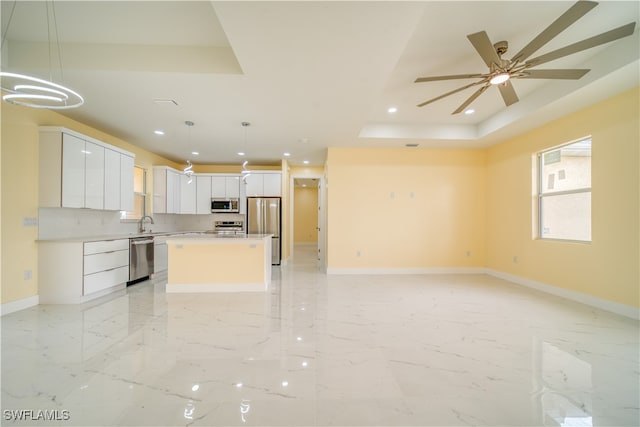 kitchen featuring stainless steel appliances, hanging light fixtures, white cabinetry, and a raised ceiling