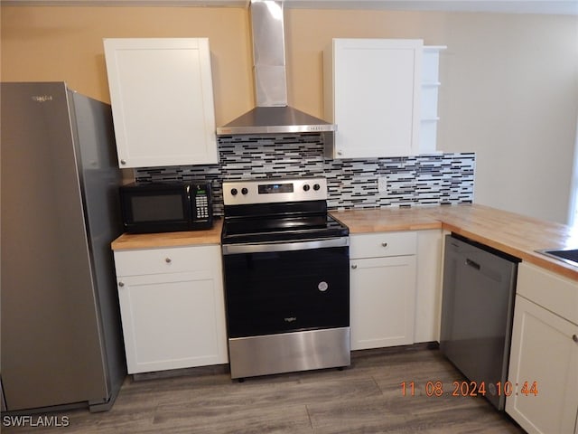 kitchen featuring butcher block counters, wall chimney exhaust hood, white cabinetry, and appliances with stainless steel finishes