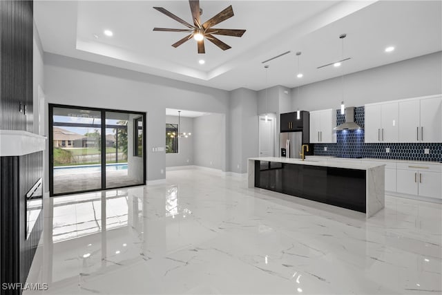 kitchen with white cabinetry, wall chimney range hood, stainless steel fridge with ice dispenser, pendant lighting, and an island with sink