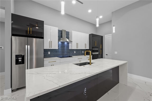 kitchen with white cabinets, hanging light fixtures, a center island with sink, and wall chimney range hood