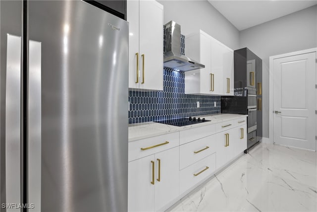 kitchen with light stone counters, white cabinets, wall chimney range hood, backsplash, and appliances with stainless steel finishes