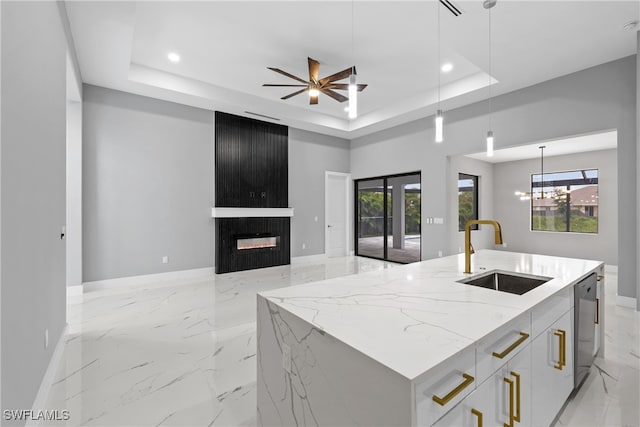 kitchen featuring sink, light stone countertops, hanging light fixtures, a kitchen island with sink, and white cabinets