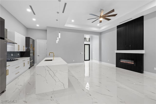 kitchen featuring white cabinets, sink, a kitchen island with sink, light stone countertops, and pendant lighting