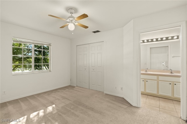 unfurnished bedroom with light carpet, ceiling fan, sink, connected bathroom, and a closet