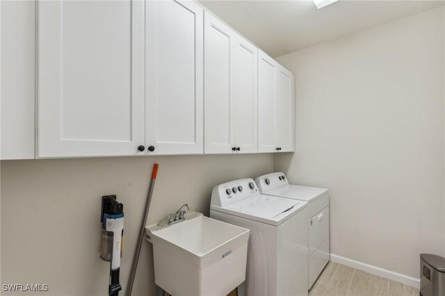 washroom with washer and dryer, baseboards, cabinet space, and a sink