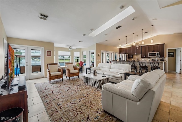 living room featuring french doors, light tile patterned floors, lofted ceiling with skylight, and ceiling fan