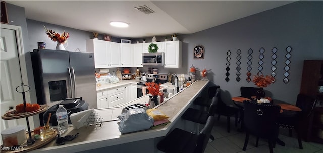 kitchen featuring stainless steel appliances, white cabinetry, kitchen peninsula, a kitchen breakfast bar, and light tile patterned floors