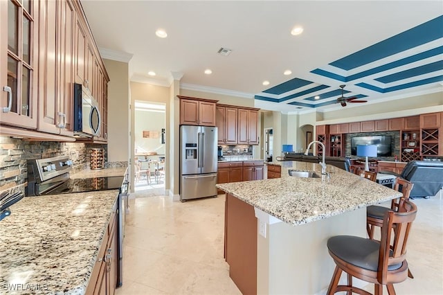 kitchen featuring a large island with sink, sink, light stone countertops, appliances with stainless steel finishes, and a breakfast bar area