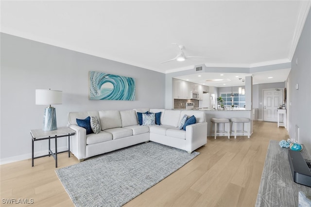 living room featuring ceiling fan, ornamental molding, and light hardwood / wood-style flooring