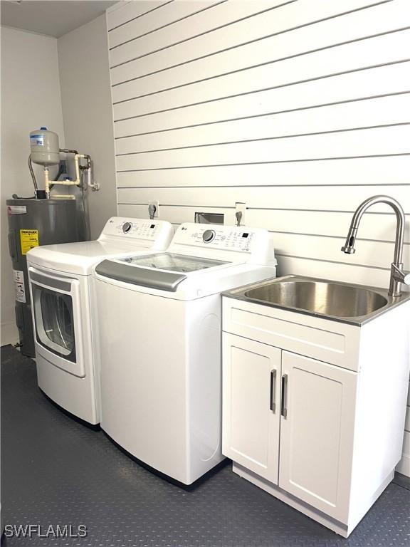 laundry area featuring sink, cabinets, water heater, independent washer and dryer, and wood walls