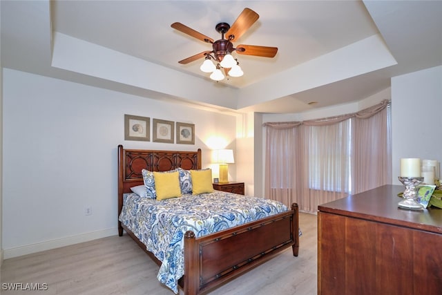 bedroom featuring a tray ceiling, light wood-style flooring, baseboards, and a ceiling fan