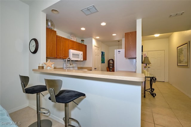 kitchen with white appliances, kitchen peninsula, light tile patterned floors, and a kitchen bar