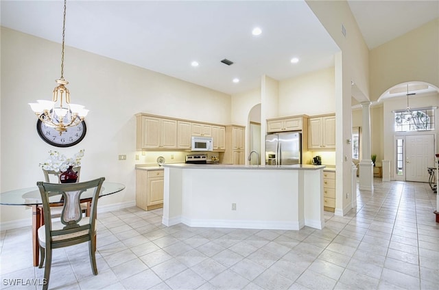 kitchen with a center island with sink, appliances with stainless steel finishes, light tile patterned floors, a towering ceiling, and a notable chandelier