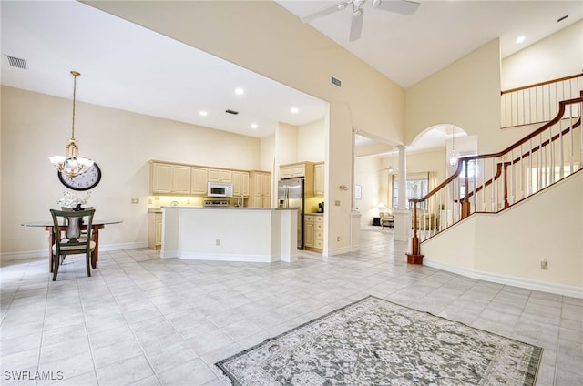 living room featuring light tile patterned flooring, ceiling fan with notable chandelier, ornate columns, and high vaulted ceiling