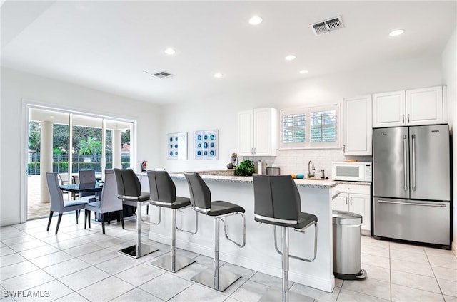 kitchen with white cabinets, plenty of natural light, light stone counters, and stainless steel refrigerator