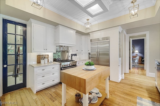 kitchen with high quality appliances, white cabinetry, decorative light fixtures, and light wood-type flooring