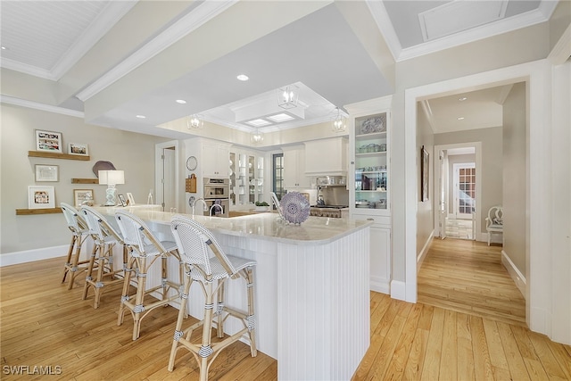 kitchen with light stone counters, double oven, light hardwood / wood-style floors, a kitchen bar, and white cabinets