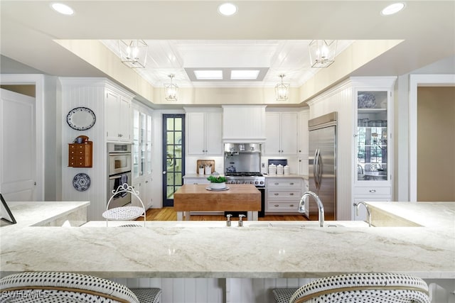 kitchen with a kitchen bar, high end appliances, decorative light fixtures, light hardwood / wood-style flooring, and white cabinetry