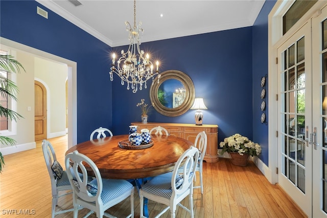 dining space with french doors, light hardwood / wood-style floors, an inviting chandelier, and ornamental molding