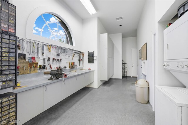 bar featuring stacked washer / drying machine, a towering ceiling, white cabinetry, and a workshop area