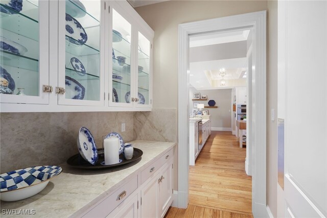 bar featuring tasteful backsplash, light stone counters, white cabinets, and light hardwood / wood-style floors