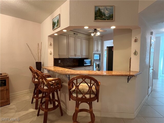 kitchen with kitchen peninsula, appliances with stainless steel finishes, a kitchen breakfast bar, ceiling fan, and decorative backsplash