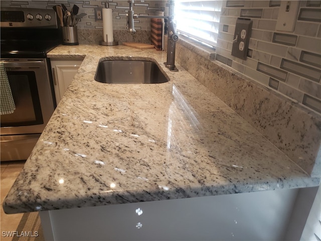 interior details featuring light stone countertops, backsplash, stainless steel range with electric cooktop, and sink