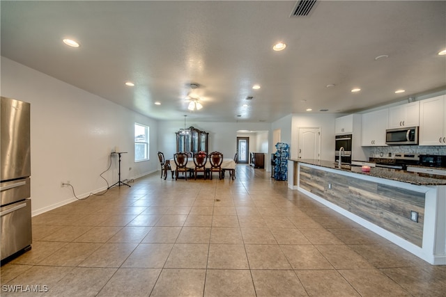 kitchen with appliances with stainless steel finishes, ceiling fan, dark stone countertops, light tile patterned floors, and white cabinets