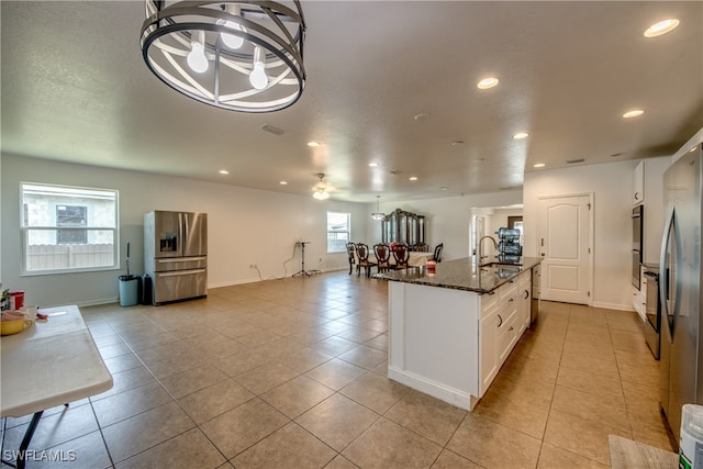 kitchen with stainless steel fridge, dark stone counters, white cabinetry, sink, and a kitchen island with sink