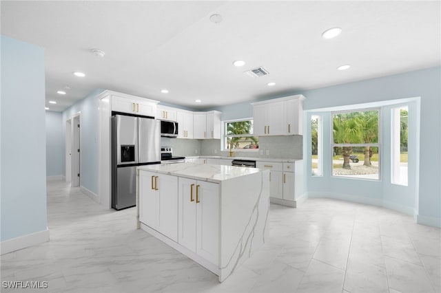 kitchen with stainless steel appliances, a center island, backsplash, light stone countertops, and white cabinetry