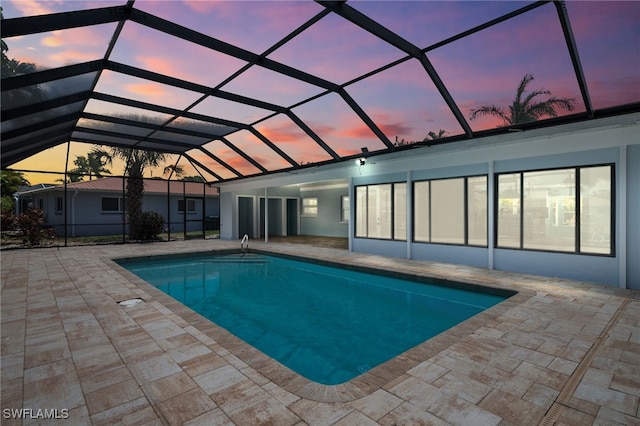 pool at dusk featuring a patio and glass enclosure