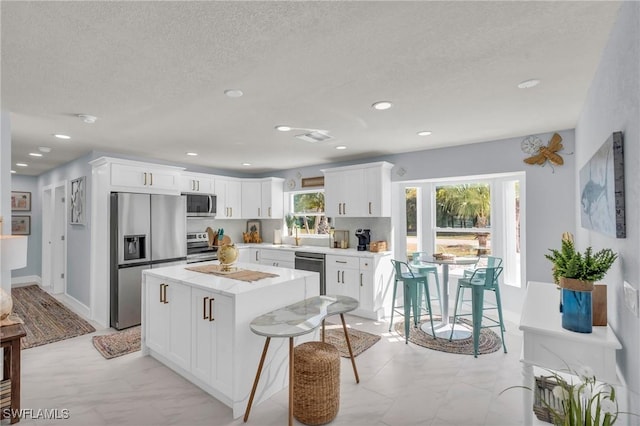 kitchen featuring a breakfast bar area, white cabinetry, a center island, a textured ceiling, and stainless steel appliances