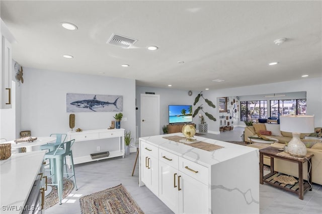 kitchen featuring a breakfast bar area, light stone countertops, white cabinets, and a kitchen island