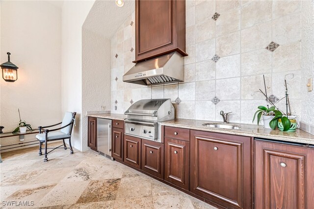 kitchen featuring light stone countertops, backsplash, sink, stainless steel refrigerator, and range hood