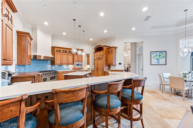 kitchen with pendant lighting, a spacious island, wall chimney range hood, ornamental molding, and appliances with stainless steel finishes