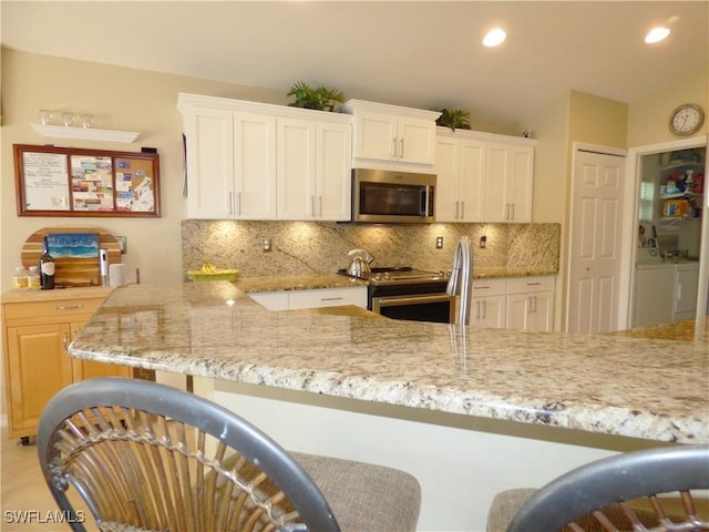 kitchen with light stone countertops, independent washer and dryer, stainless steel appliances, and white cabinetry