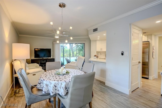 dining area featuring light wood-type flooring, a notable chandelier, crown molding, and sink