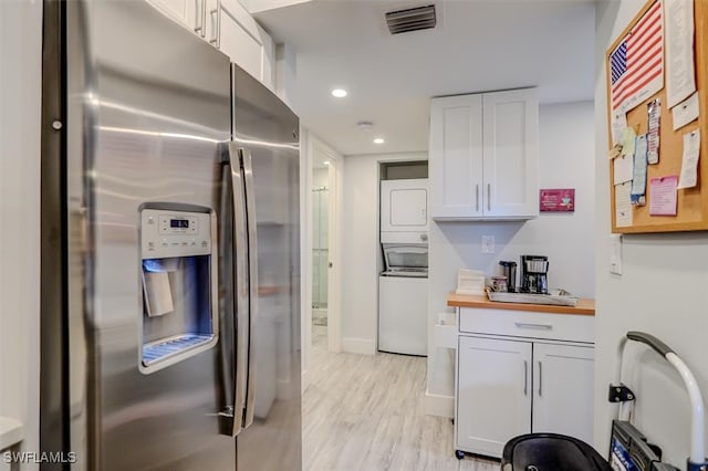 kitchen featuring butcher block counters, light hardwood / wood-style flooring, stainless steel refrigerator with ice dispenser, stacked washer / dryer, and white cabinets