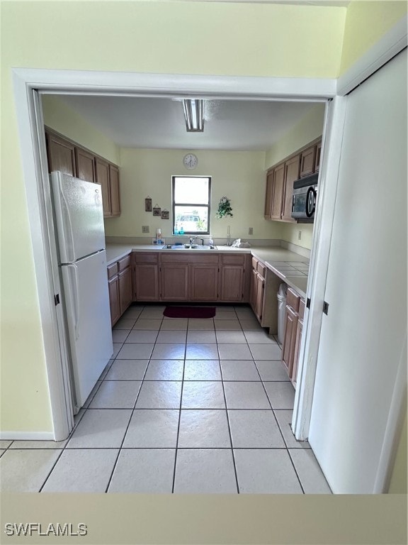 kitchen with white refrigerator, light tile patterned floors, and sink