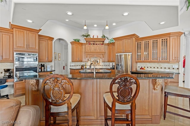 kitchen featuring dark stone countertops, backsplash, a kitchen island with sink, and stainless steel appliances